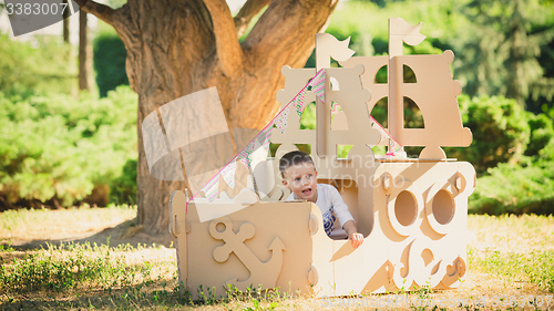 Image of Boy playing in cardboard boat at park.