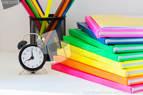 Image of Black alarm clock. Multi colored books in stack
