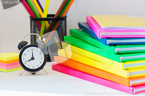 Image of Black alarm clock and multi colored books in stack