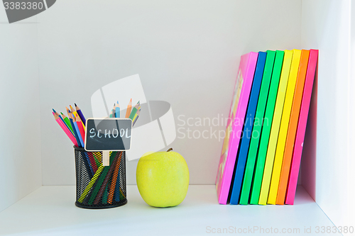 Image of Yellow apple, pencils in holder and multi colored books 