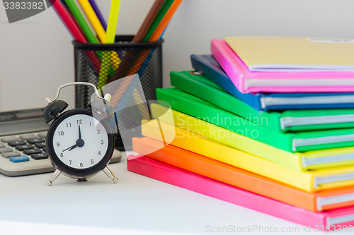 Image of Black alarm clock and multi colored books in stack