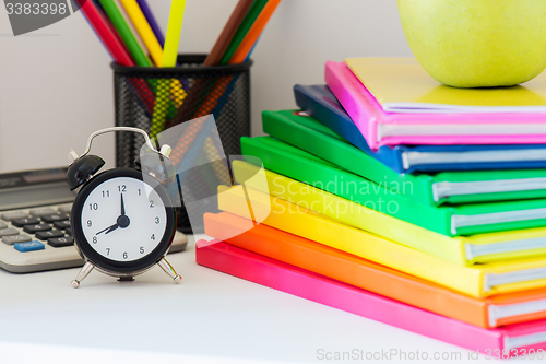 Image of Black alarm clock and multi colored books in stack