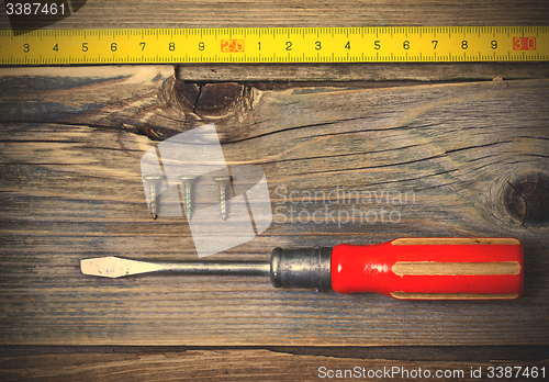 Image of old screwdriver, three screws and measuring tape on textured boa
