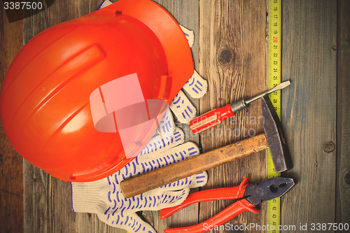 Image of aged hammer, pliers, screwdriver, tape measure, a bright helmet 