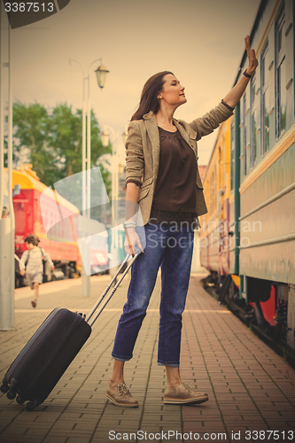 Image of woman with luggage waves his hand near passenger railcar 