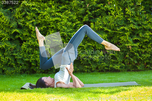 Image of woman doing yoga on a green grass at summer day
