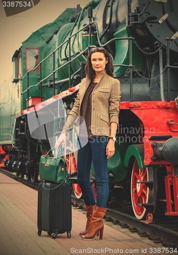 Image of adult woman traveler with a suitcase near the vintage steam loco