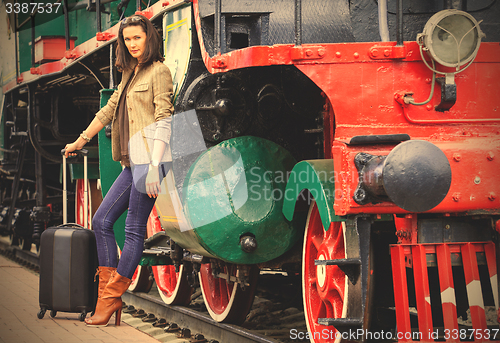 Image of woman traveler with a suitcase near the old steam locomotive