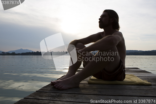 Image of Young man sitting at a bridge in evening light