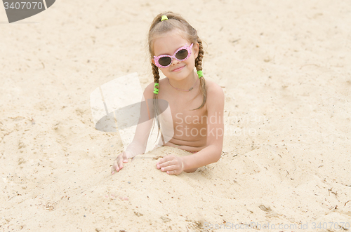 Image of Five-year girl with glasses on beach covered with sand up to his waist