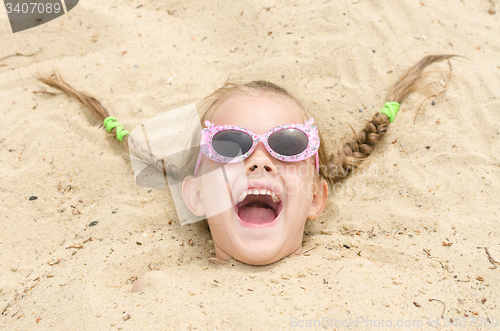 Image of Five-year girl with glasses on a beach strewn on his head in the sand