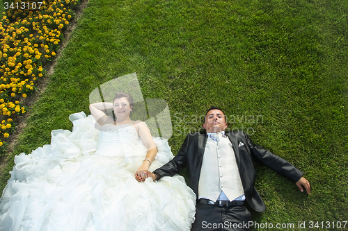 Image of Bride and groom holding hands on lawn with flowers