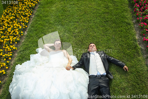 Image of Bride and groom lying on lawn with flowers