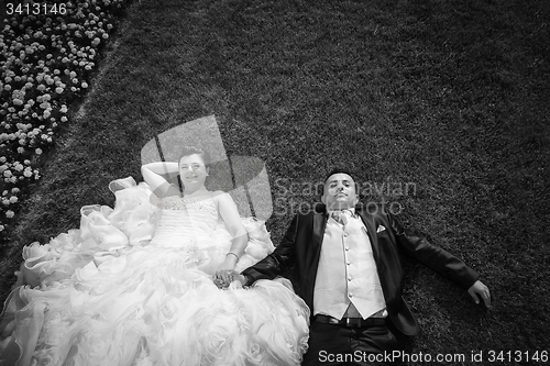 Image of Bride and groom holding hands on lawn with flowers bw