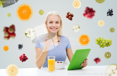 Image of smiling woman with tablet pc eating breakfast