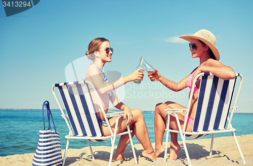 Image of happy women clinking bottles and drinking on beach