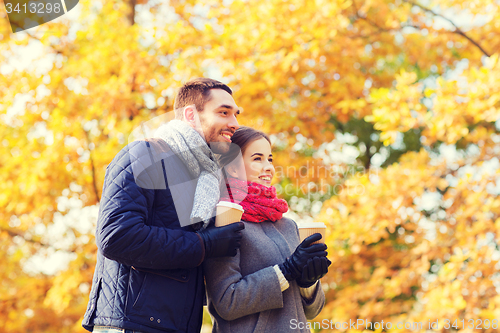 Image of smiling couple with coffee cups in autumn park