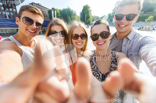 Image of happy friends taking selfie and showing thumbs up