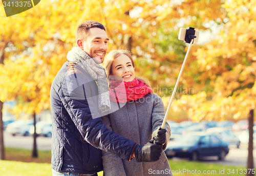 Image of smiling couple with smartphone in autumn park