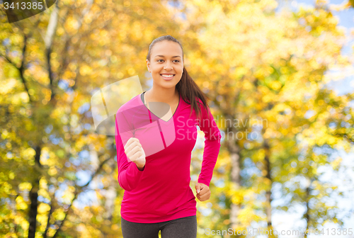 Image of smiling woman running outdoors at autumn