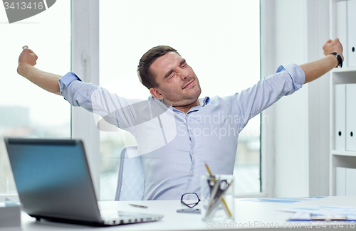Image of bored businessman with laptop and papers at office