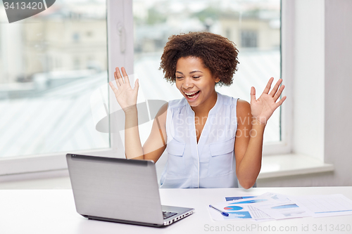 Image of happy african woman with laptop at office