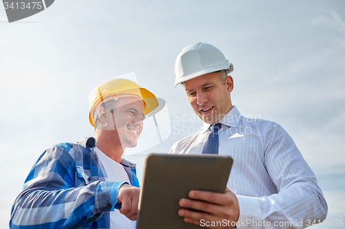 Image of happy builders in hardhats with tablet pc outdoors