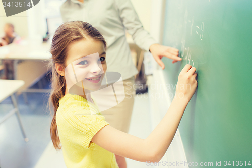 Image of little smiling schoolgirl writing on chalk board