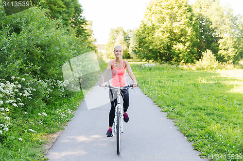 Image of happy young woman riding bicycle outdoors