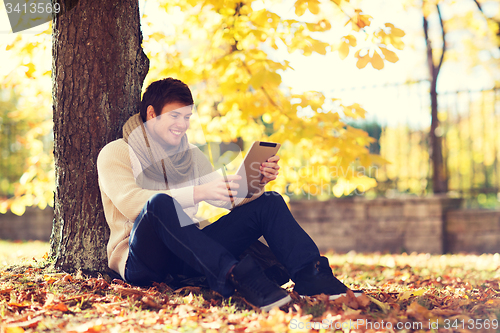 Image of smiling young man with tablet pc in autumn park