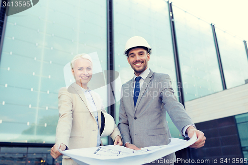 Image of smiling businessmen with blueprint and helmets