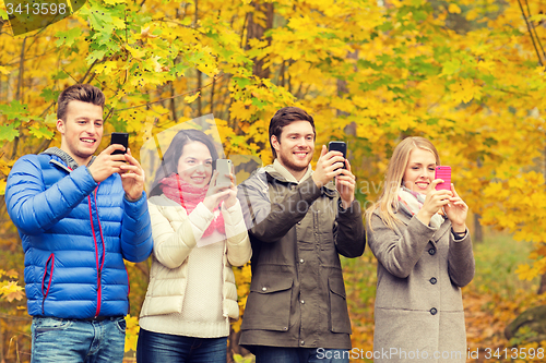 Image of smiling friends with smartphones in city park