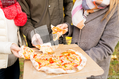 Image of close up of friends hands eating pizza outdoors