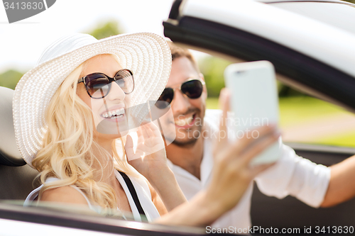 Image of happy couple in car taking selfie with smartphone