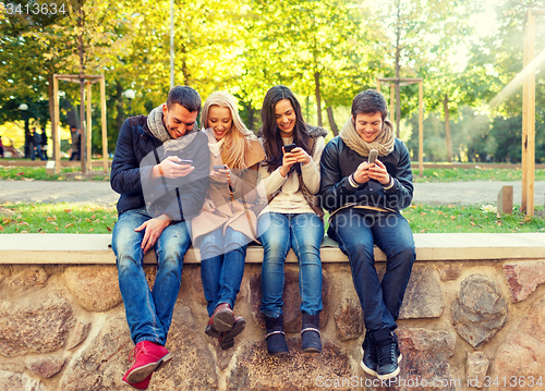 Image of smiling friends with smartphones in city park