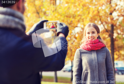 Image of smiling couple with smartphone in autumn park