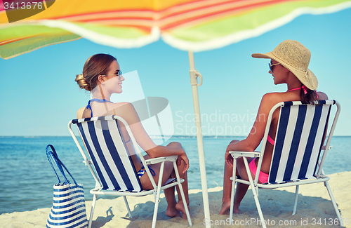 Image of happy women sunbathing in lounges on beach