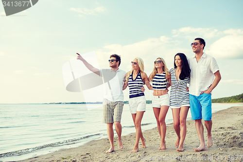 Image of smiling friends in sunglasses walking on beach
