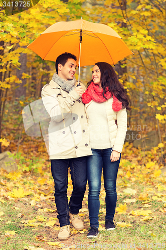 Image of smiling couple with umbrella in autumn park