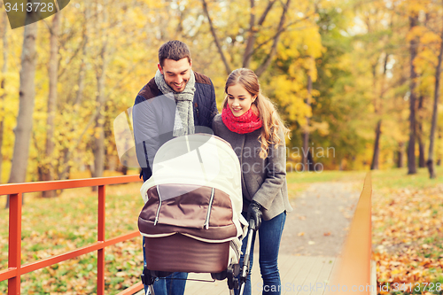 Image of smiling couple with baby pram in autumn park