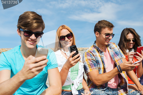 Image of group of happy friends with smartphones outdoors