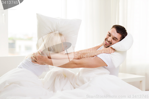 Image of happy couple having pillow fight in bed at home