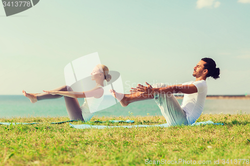 Image of smiling couple making yoga exercises outdoors