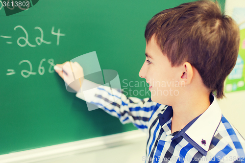 Image of little smiling schoolboy writing on chalk board