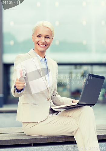 Image of smiling businesswoman working with laptop outdoors