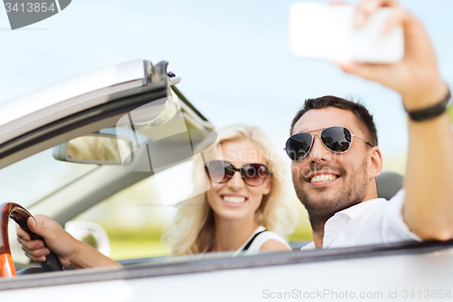 Image of happy couple in car taking selfie with smartphone