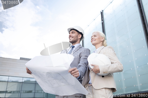 Image of smiling businessmen with blueprint and helmets