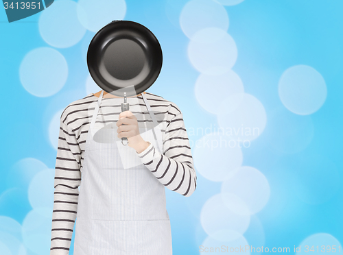 Image of man or cook in apron hiding face behind frying pan