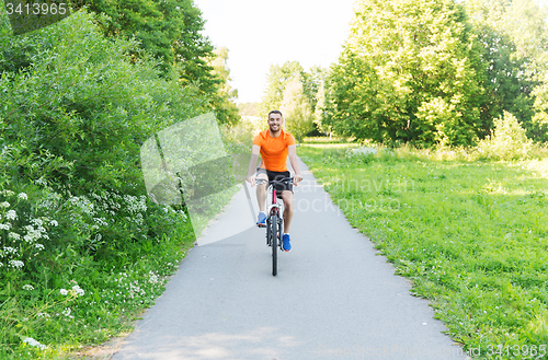 Image of happy young man riding bicycle outdoors