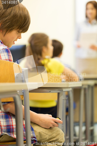 Image of school boy with smartphone on lesson at classroom